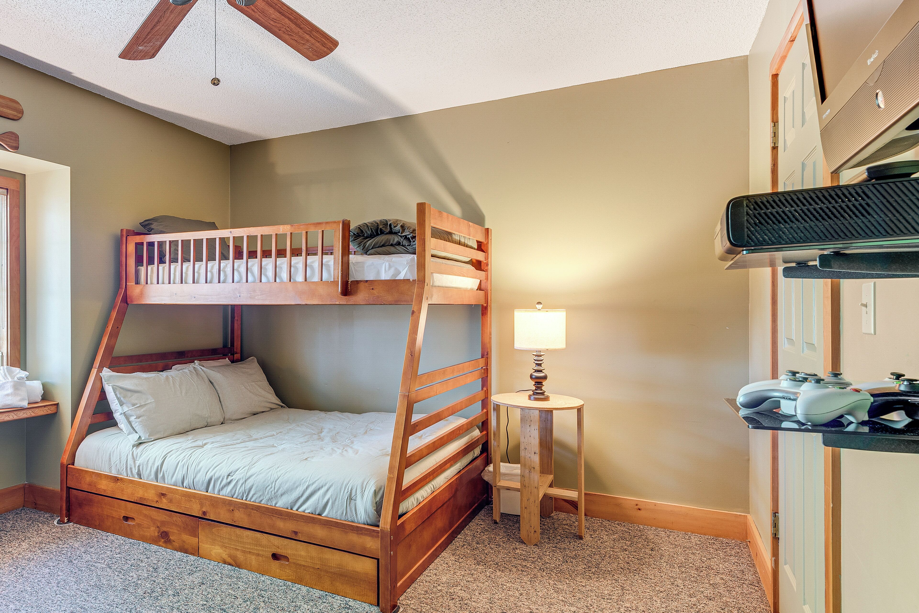 A bunk bed with a wooden frame, a small bedside table with a lamp, and a shelf with electronic devices.