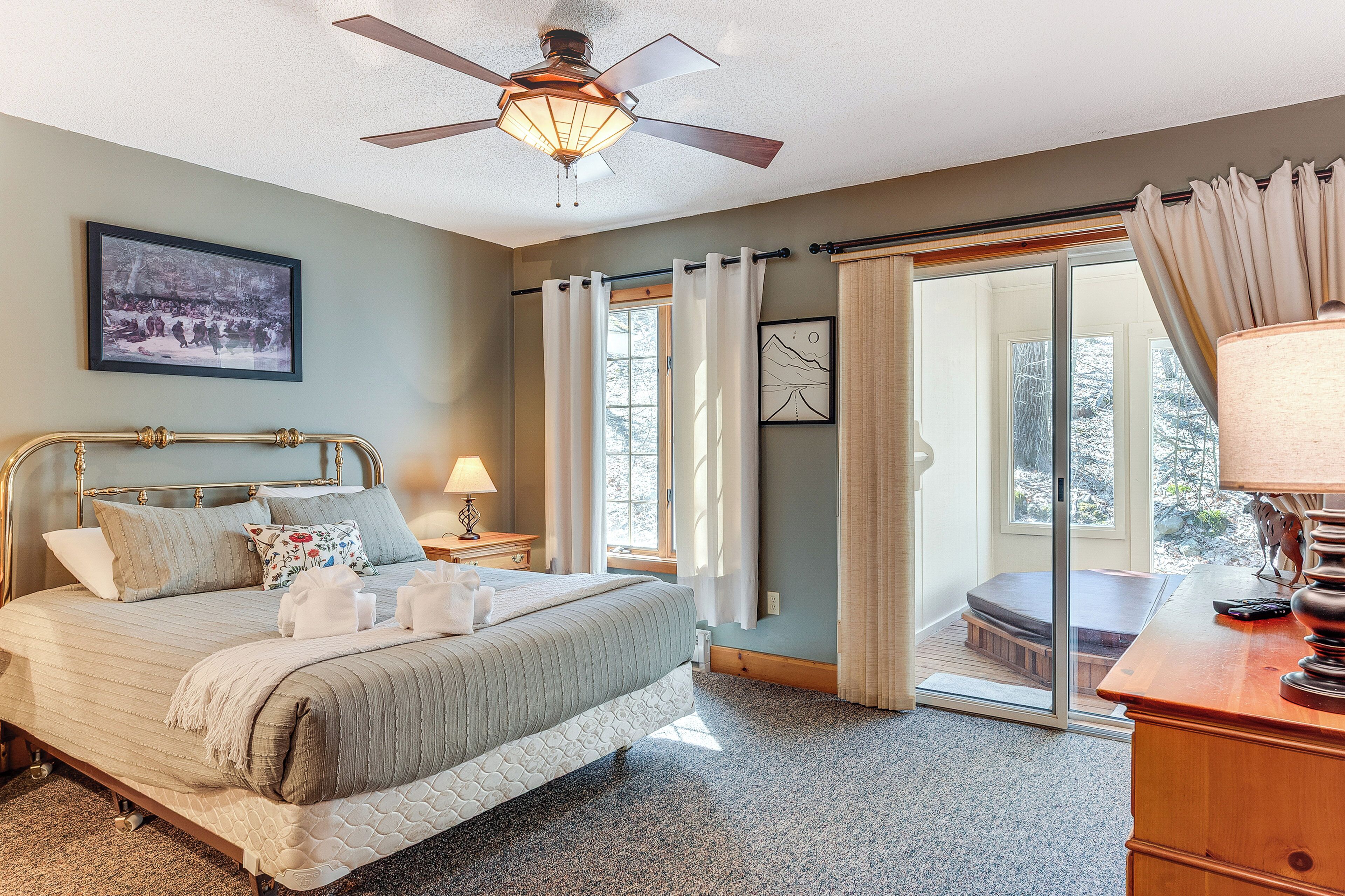 A bedroom with a bed, a ceiling fan, a window with curtains, a framed picture on the wall, and a view of the outdoors.