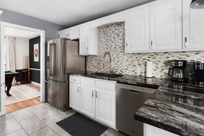 A modern kitchen with white cabinets, a stainless steel refrigerator, a dishwasher, and a coffee maker.