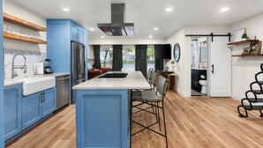 A modern kitchen with blue cabinets, a central island, and a dining area. - Upscale Retreat: Pool, Hot Tub, Gym & Games (Round Rock)