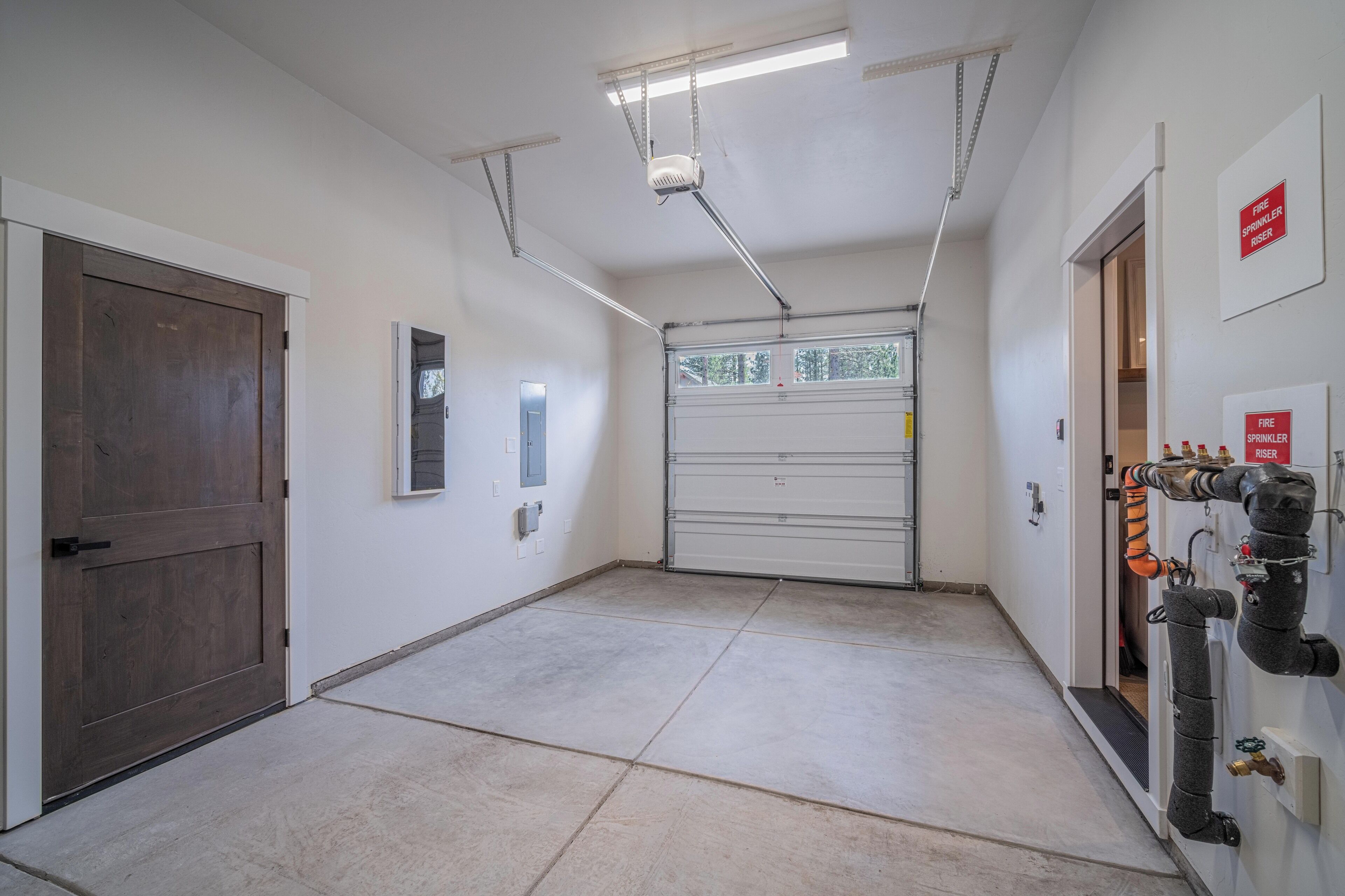 A clean, well-lit hallway with a garage door, a fire sprinkler system, and a wooden door.