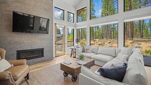 Un salon moderne doté d’une cheminée, de grandes fenêtres et offrant une vue sur une forêt.