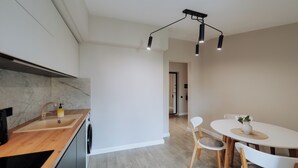 Una cocina moderna con encimera de madera, lavavajillas integrado y un lavamanos. Hay una zona de comedor con una mesa y sillas blancas, y un aplique de techo.