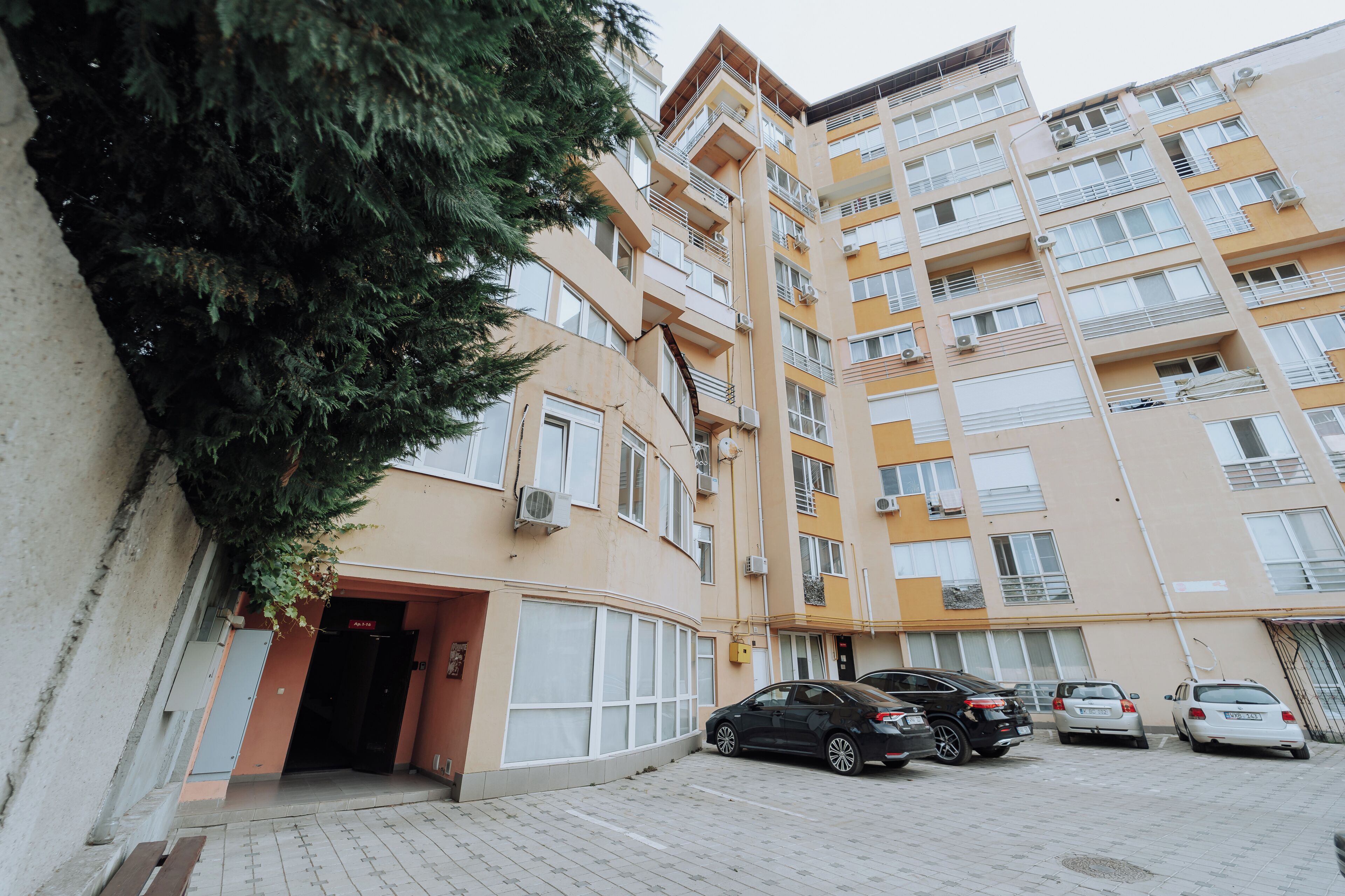 A multi-story residential building with a curved entrance, several balconies, and parked cars.