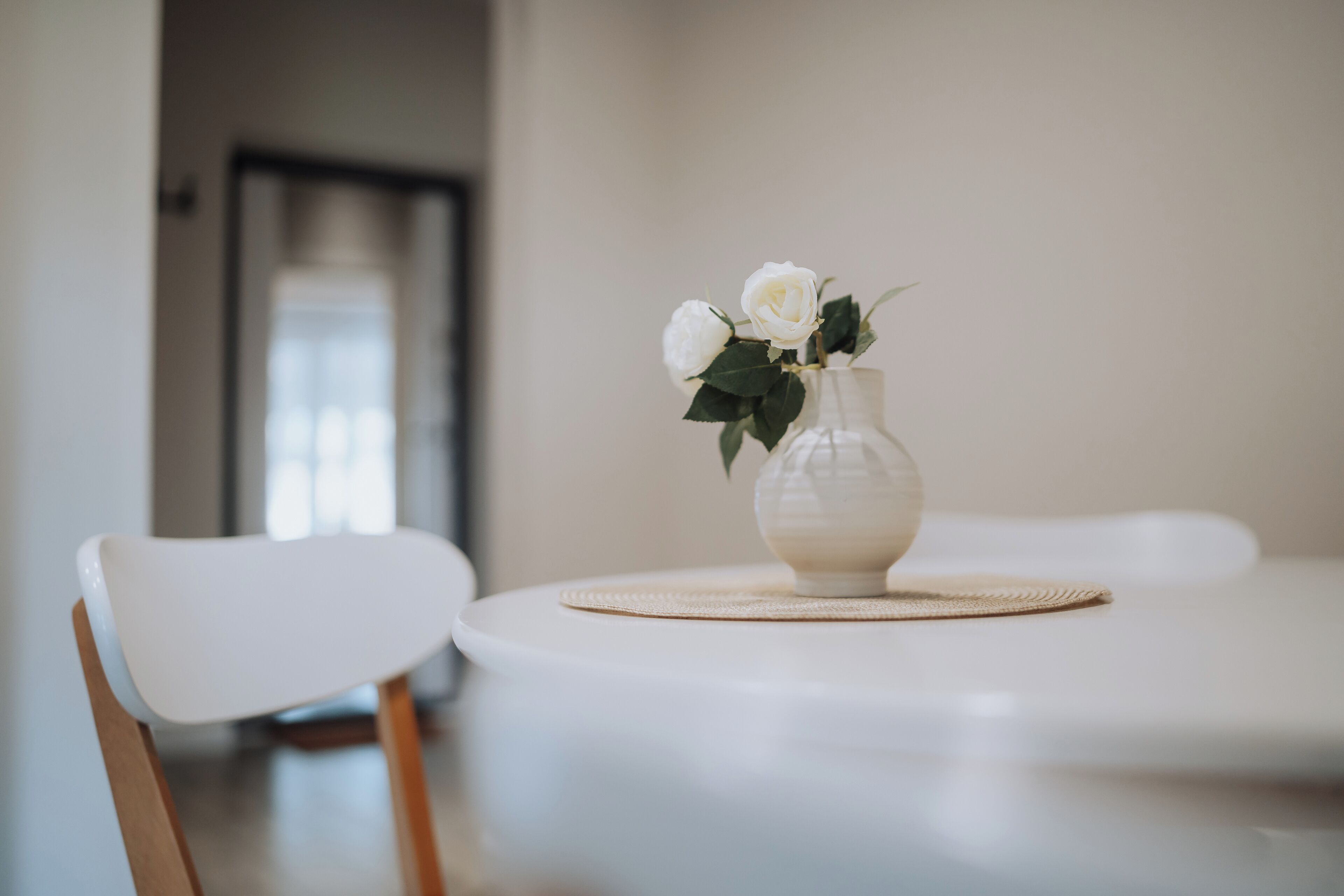 A white chair and a round table with a vase containing white flowers.