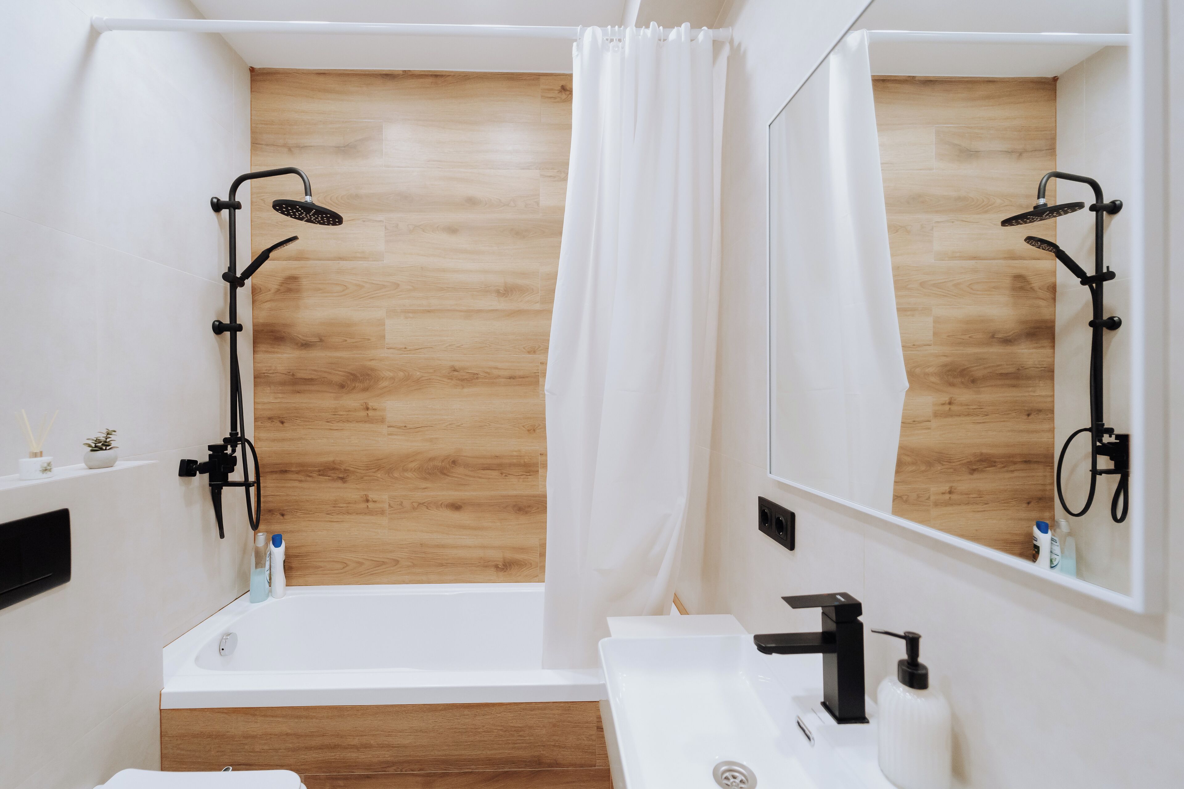 Un bagno moderno con pavimento in legno, una vasca da bagno bianca, un lavandino con rubinetto nero e una doccia con soffione nero.