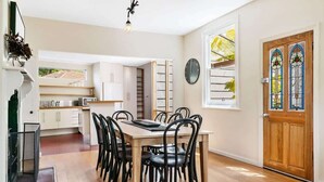 A modern kitchen with a dining table and chairs, a clock, and a wooden door with stained glass.