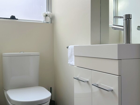 Un baño moderno con un inodoro blanco, un lavamanos con espejo y una ventana sobre el inodoro.