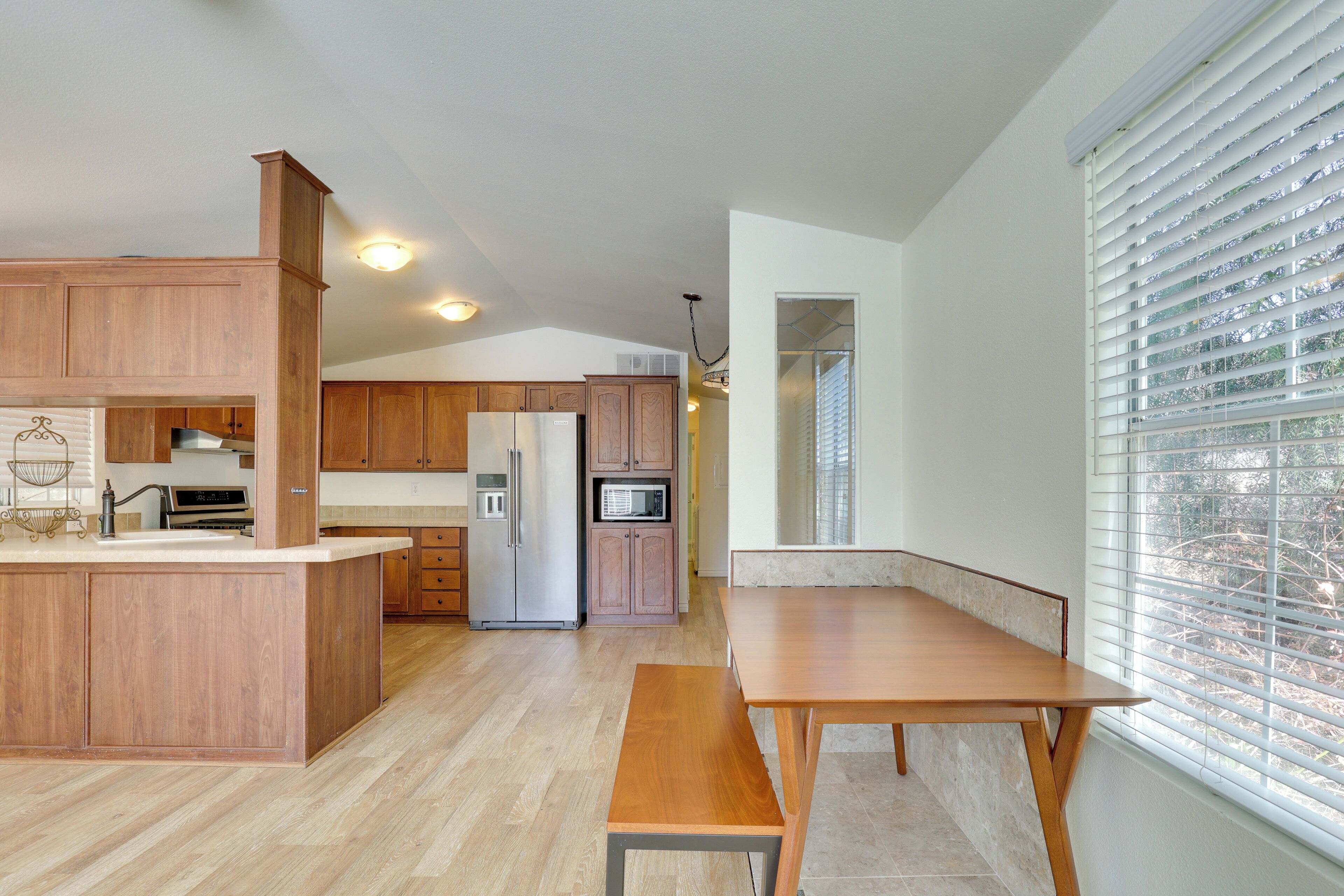 A modern kitchen with wooden cabinets, a built-in island, stainless steel appliances, and a large window with blinds.