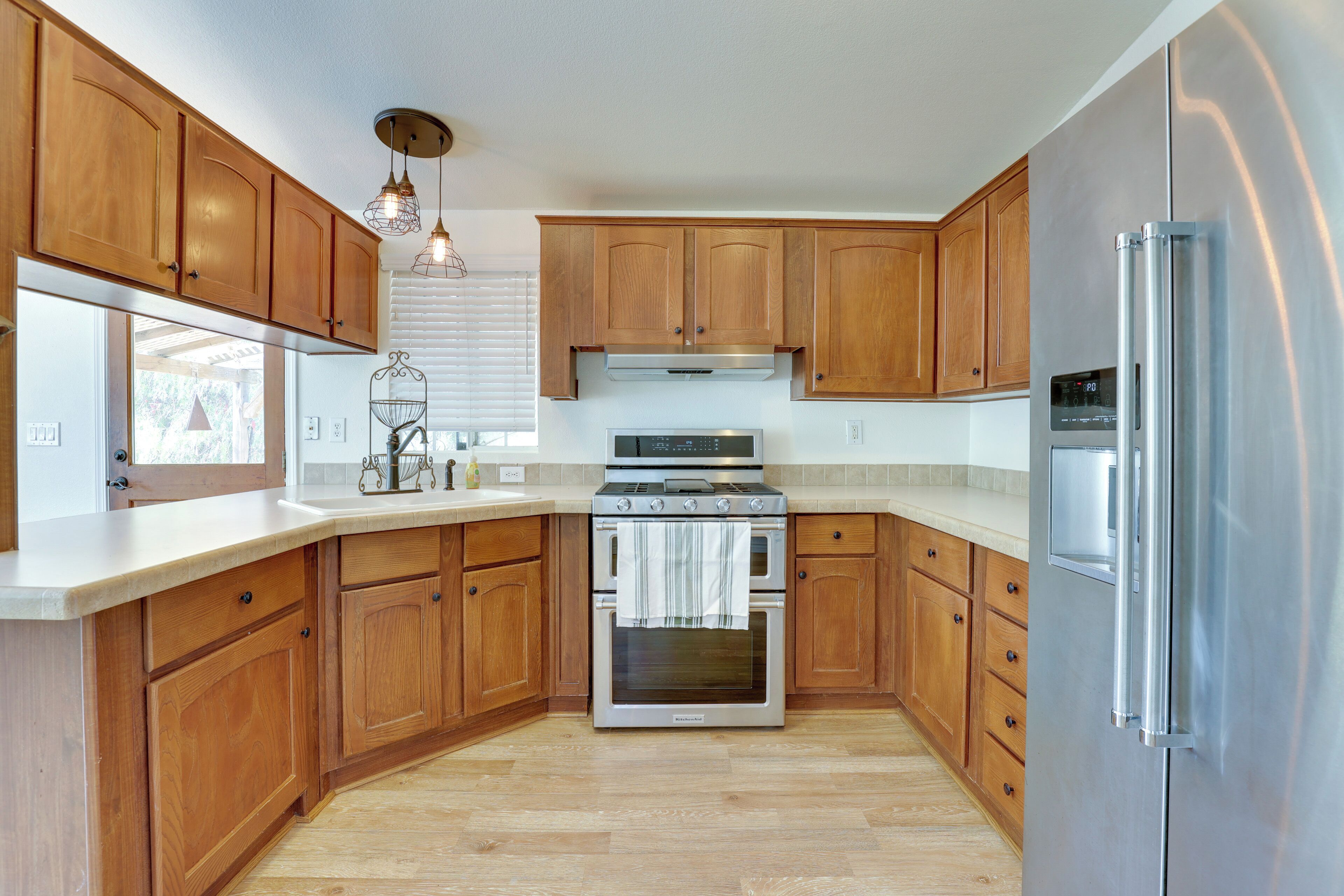 Una cocina con armarios de madera, electrodomésticos de acero inoxidable y una encimera de color claro.