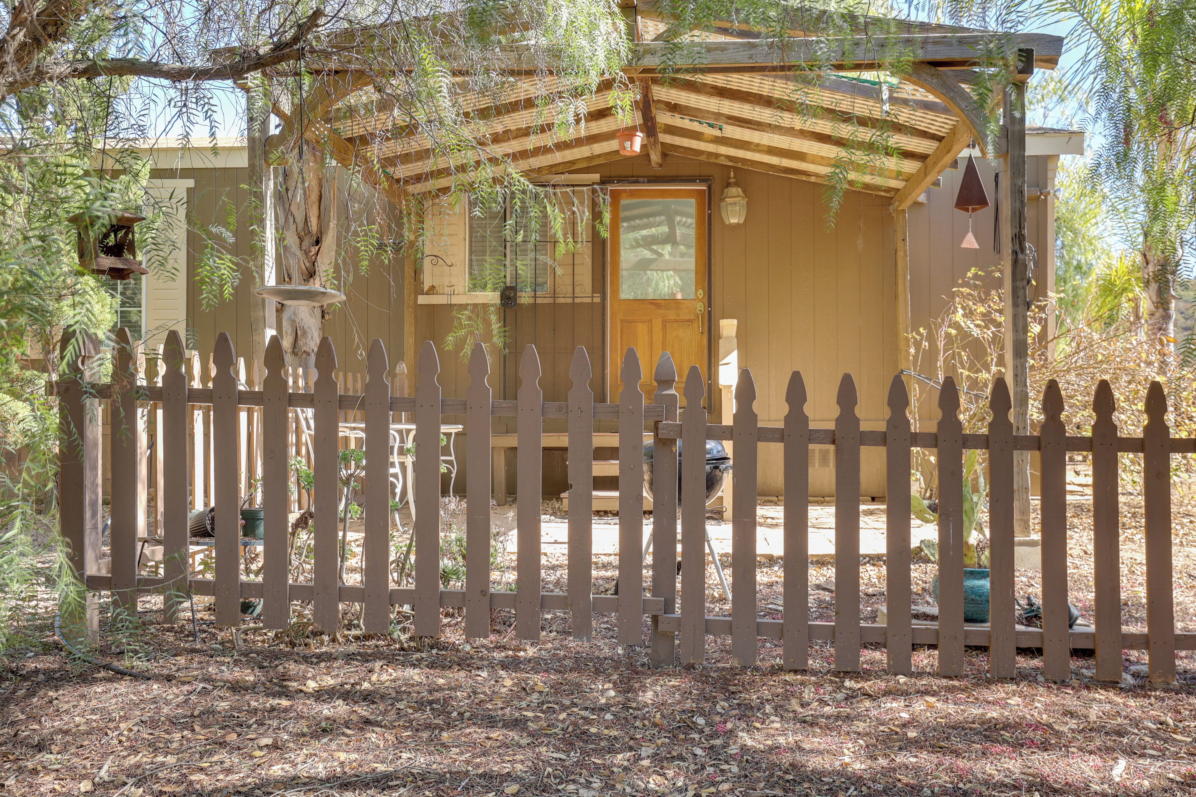 A wooden cabin with a fenced yard, a porch, and a small attached structure.