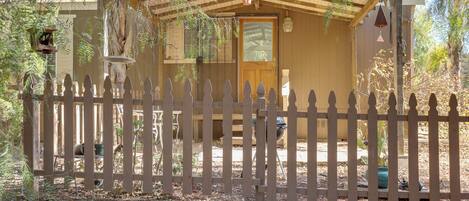A wooden cabin with a fenced yard, a porch, and a small attached structure.