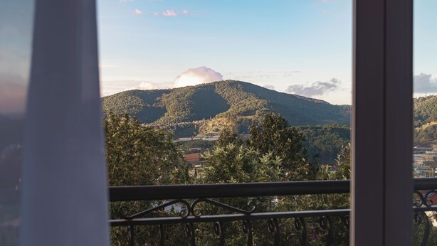 Vista desde un balcón con baranda de metal, que se extiende sobre un paisaje montañoso bajo un cielo despejado con nubes dispersas.
