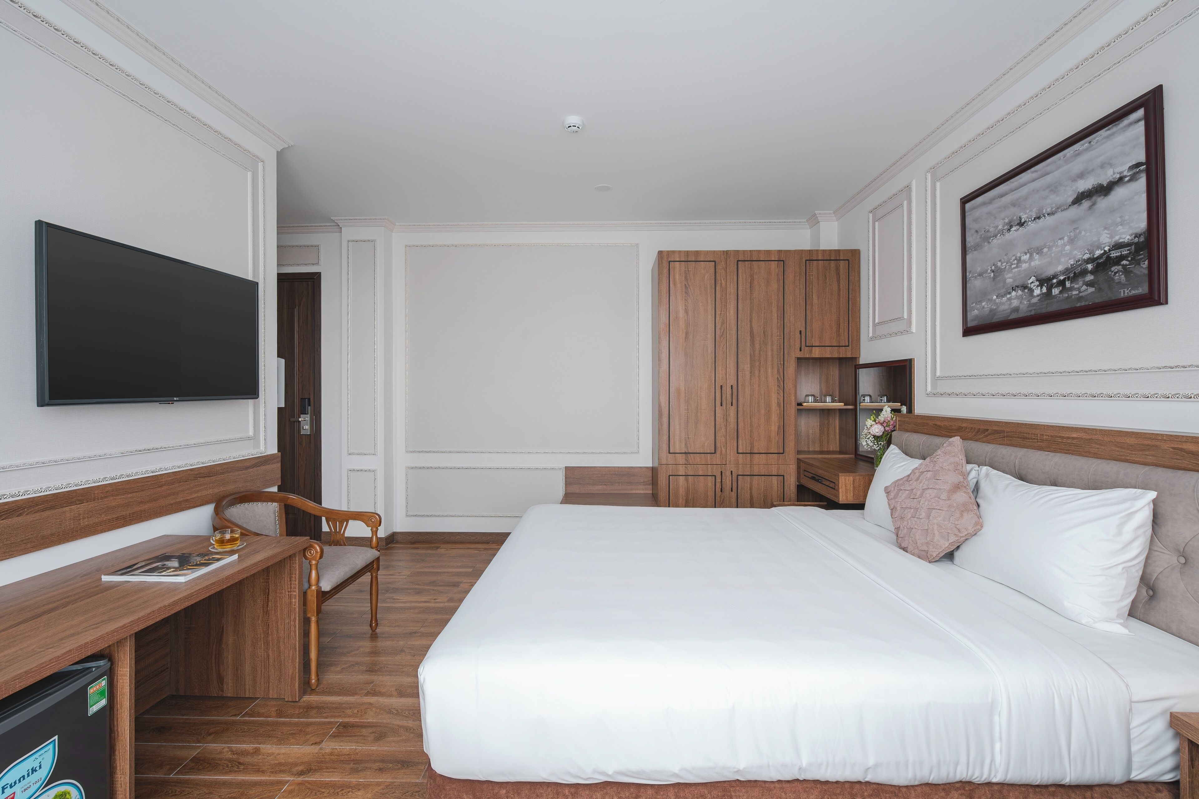 Une chambre d’hôtel avec un grand lit, un bureau en bois, une télévision et une armoire.