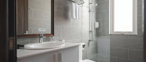 A modern bathroom with a white sink, mirror, and toilet, a glass shower enclosure, and a window providing natural light.