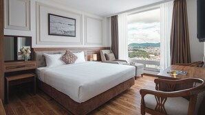 Habitación de hotel con una cama grande, un escritorio, una silla, un televisor y una ventana con vistas a la ciudad.