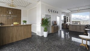Un hall d'hôtel avec un comptoir d'accueil en bois, une plante en pot et une vue sur la ville grâce à de grandes fenêtres.