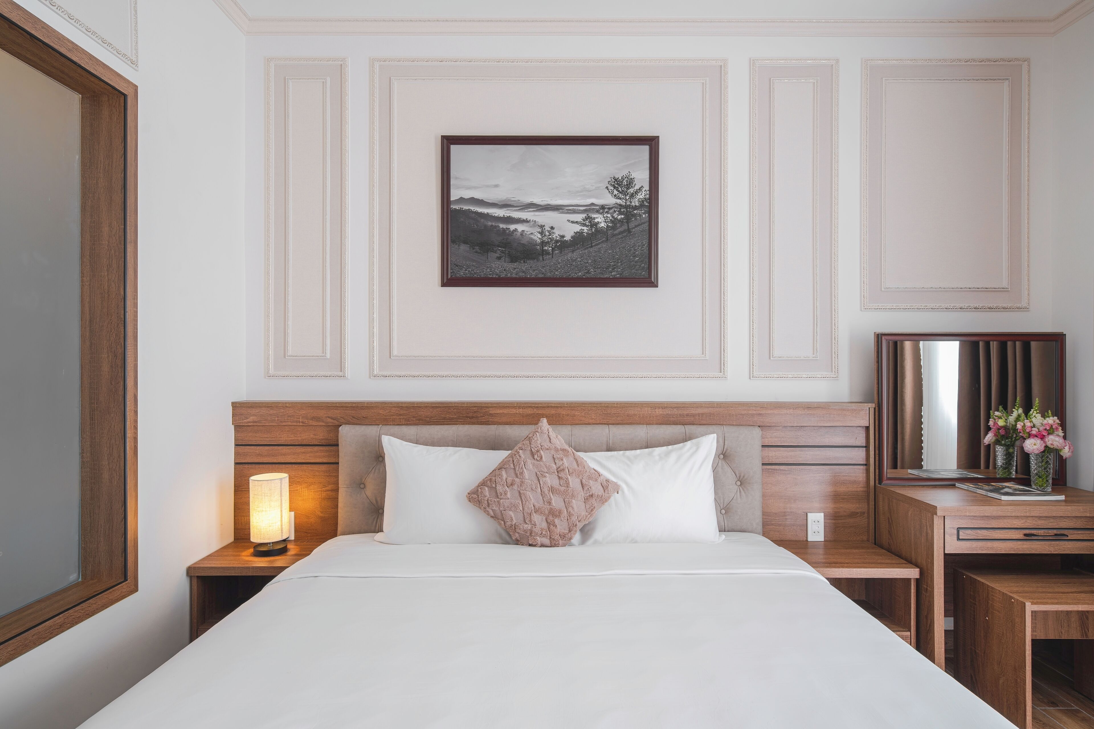 A neatly arranged hotel room with a bed, bedside table, lamp, and a framed picture on the wall.
