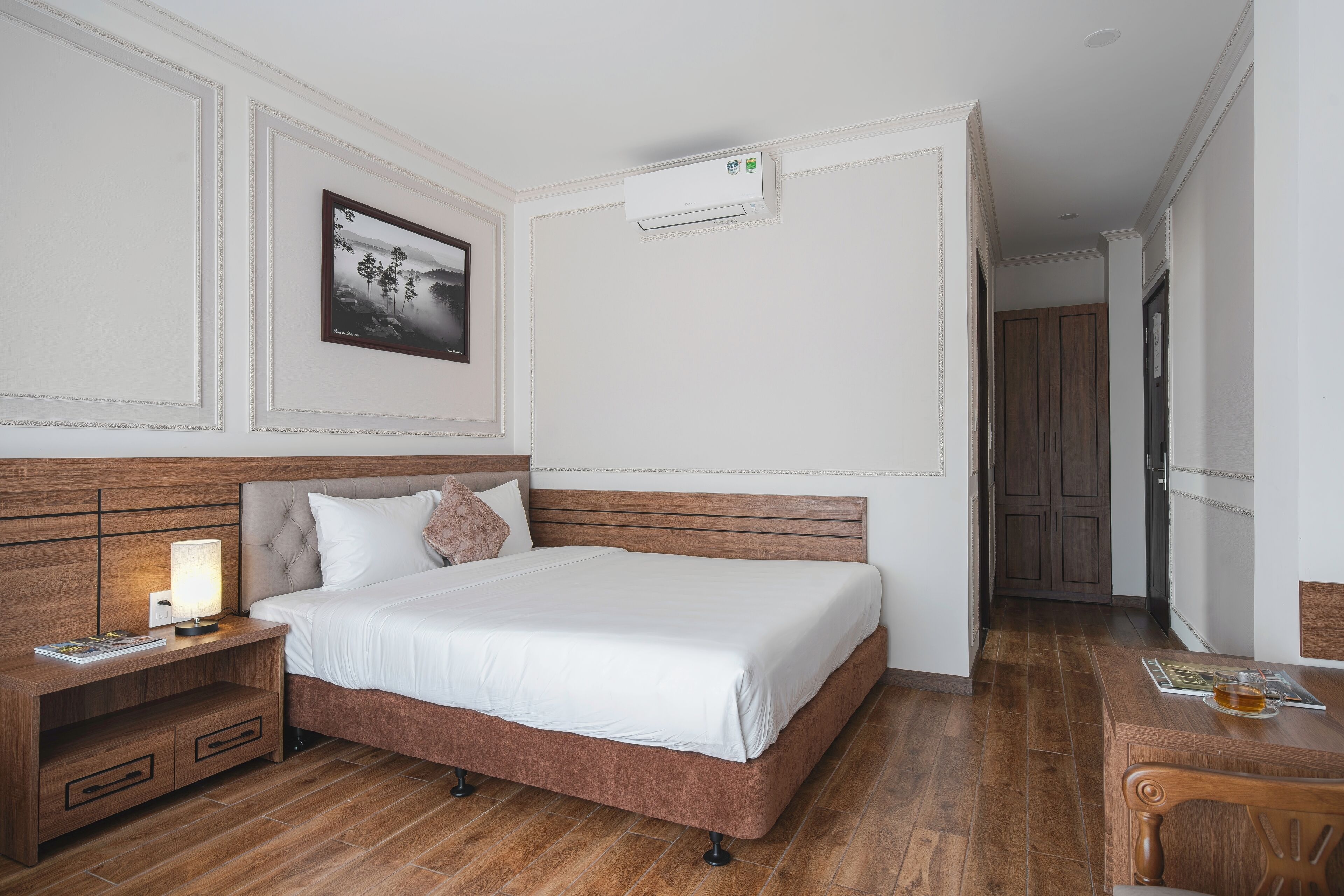 Quarto bem arrumado com cama, mesa de cabeceira e um quadro na parede.