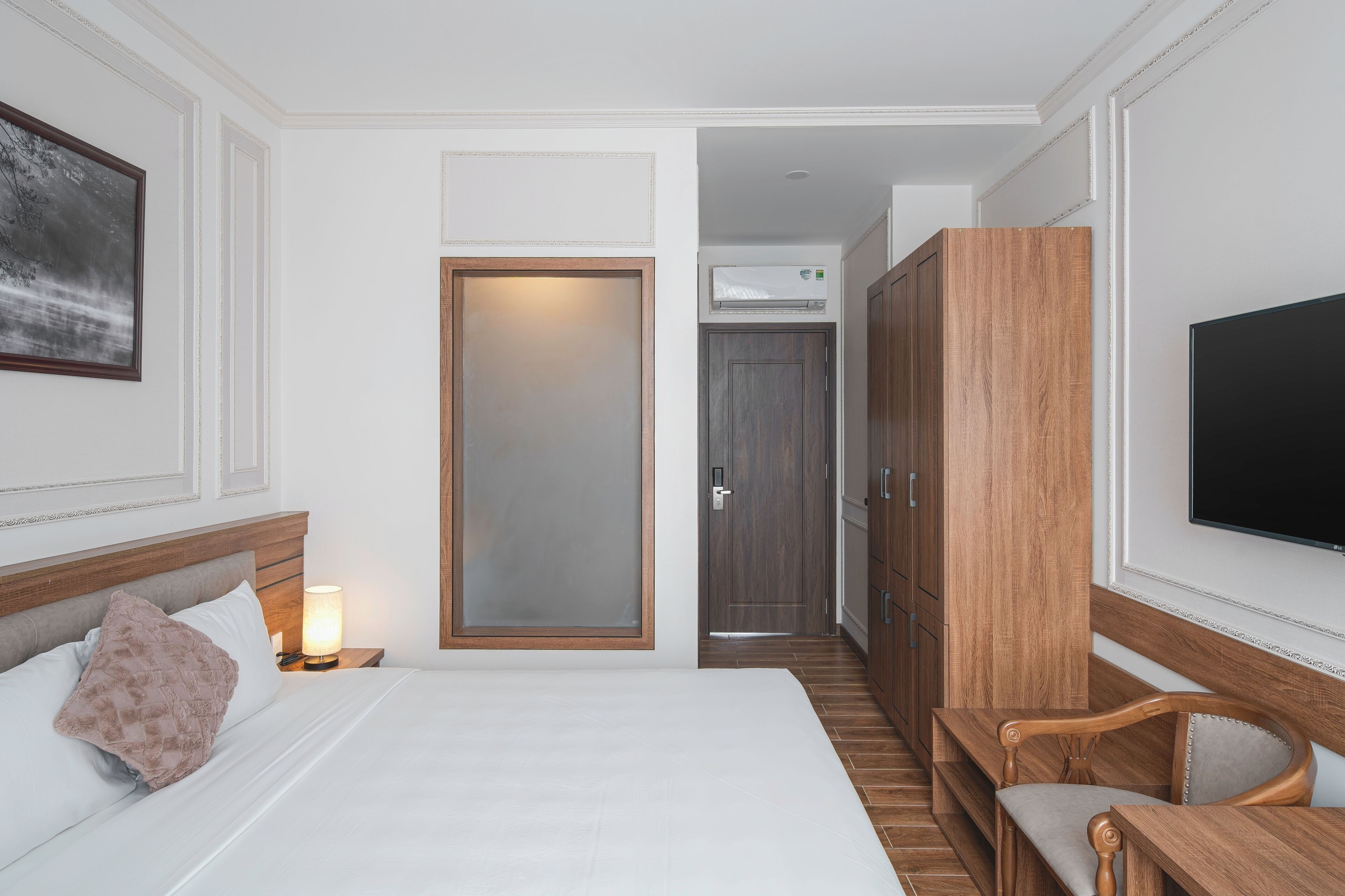 A hotel room with a bed, bedside lamp, wooden wardrobe, and a TV mounted on the wall.
