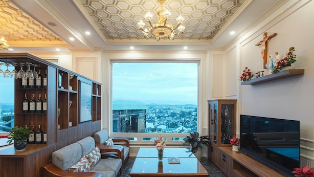 Un salon spacieux doté d’une grande fenêtre offrant une vue sur la ville, d’un meuble de rangement en bois et d’un coin salon confortable.