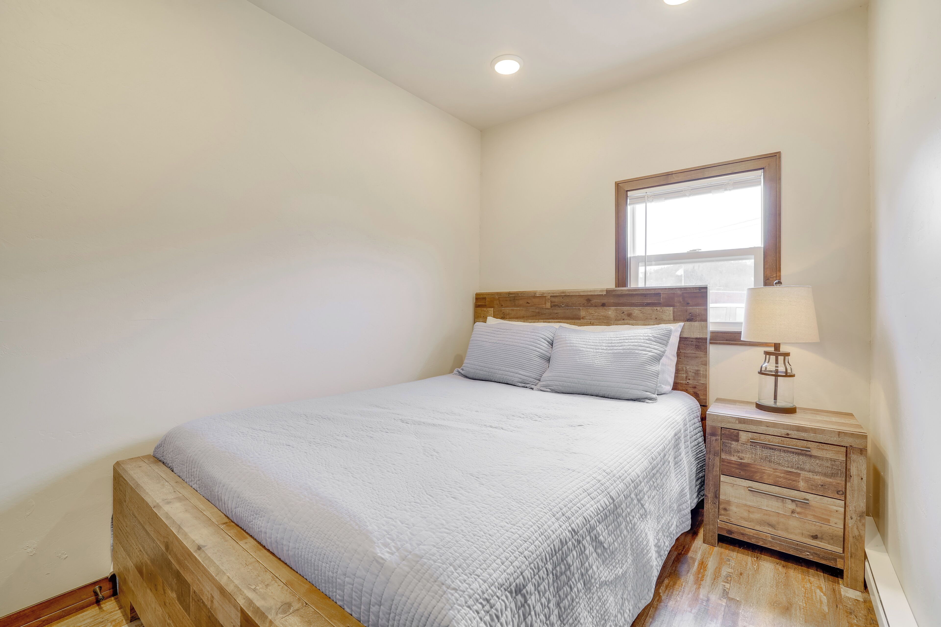 Een slaapkamer met een houten bedframe, een nachtkastje met een lamp en een raam met jaloezieën.