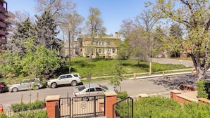 Un parking clos, avec une entrée en briques, situé à côté d’une route où sont garées des voitures et où se trouve un grand arbre.