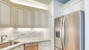 Une cuisine dotée de meubles blancs, d’un réfrigérateur en acier inoxydable, d’un dosseret en carreaux disposés en motif chevron et d’un robinet moderne.