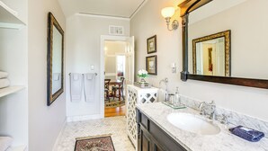 Une salle de bain avec un grand miroir, un lavabo et un meuble-lavabo. Des serviettes sont accrochées au mur, et il y a une petite table avec un vase.