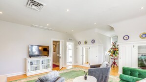 Un salon spacieux avec un téléviseur à écran plat, un canapé vert, un fauteuil gris et une table basse ronde.