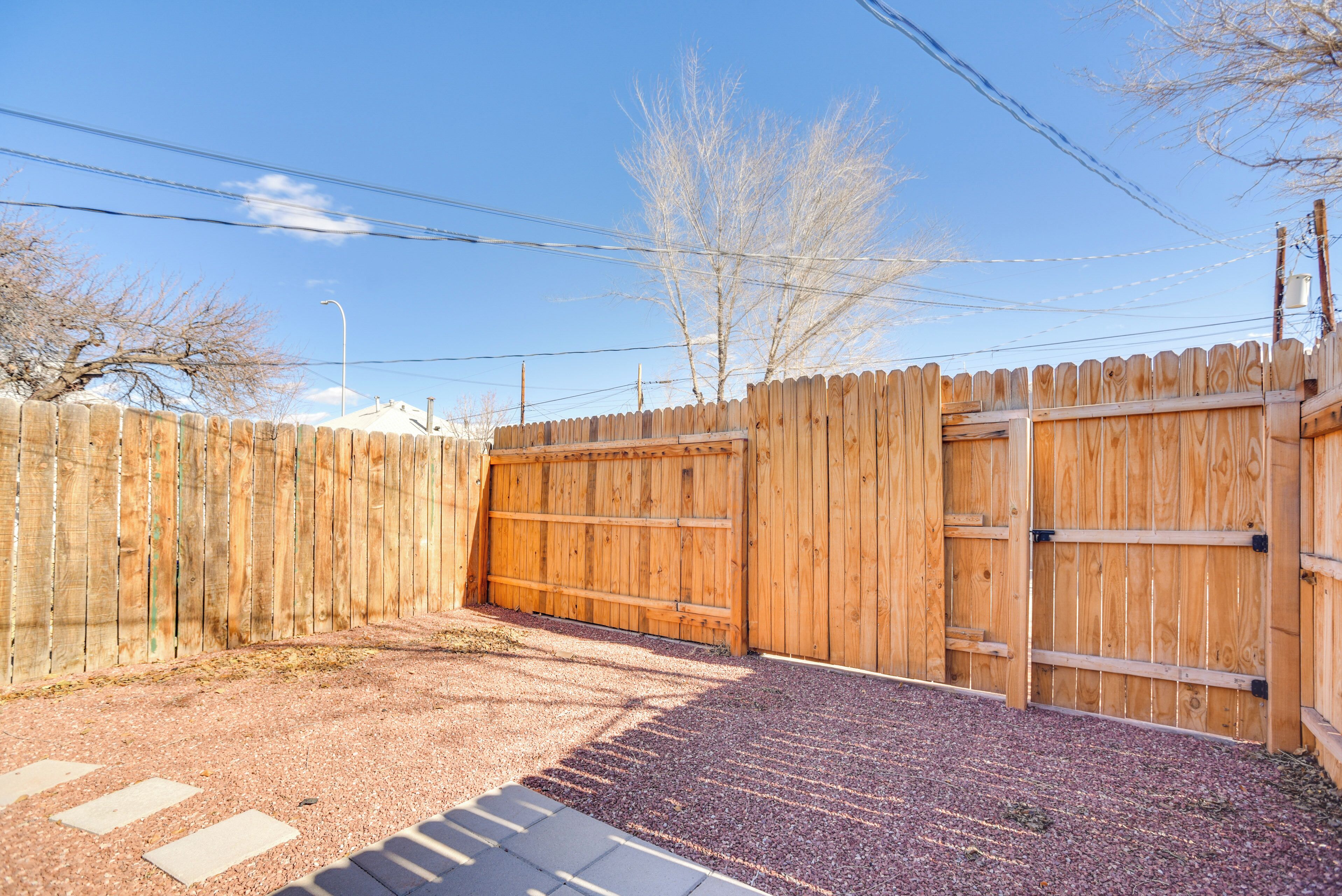 A wooden fence with a gated entrance, gravel driveway, and a clear sky.