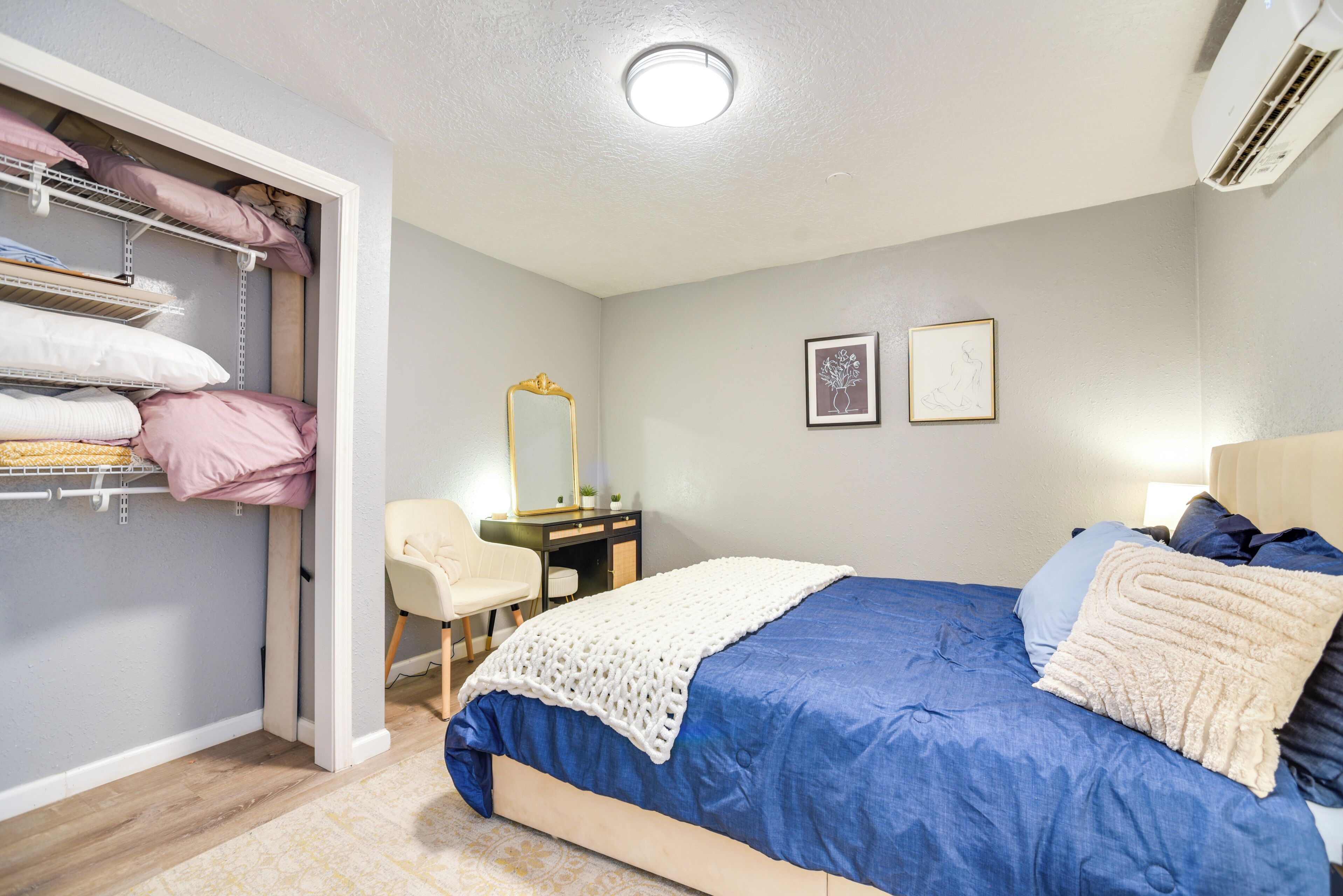 Une chambre à coucher avec un lit, une armoire avec des étagères, un bureau et deux tableaux encadrés accrochés au mur.