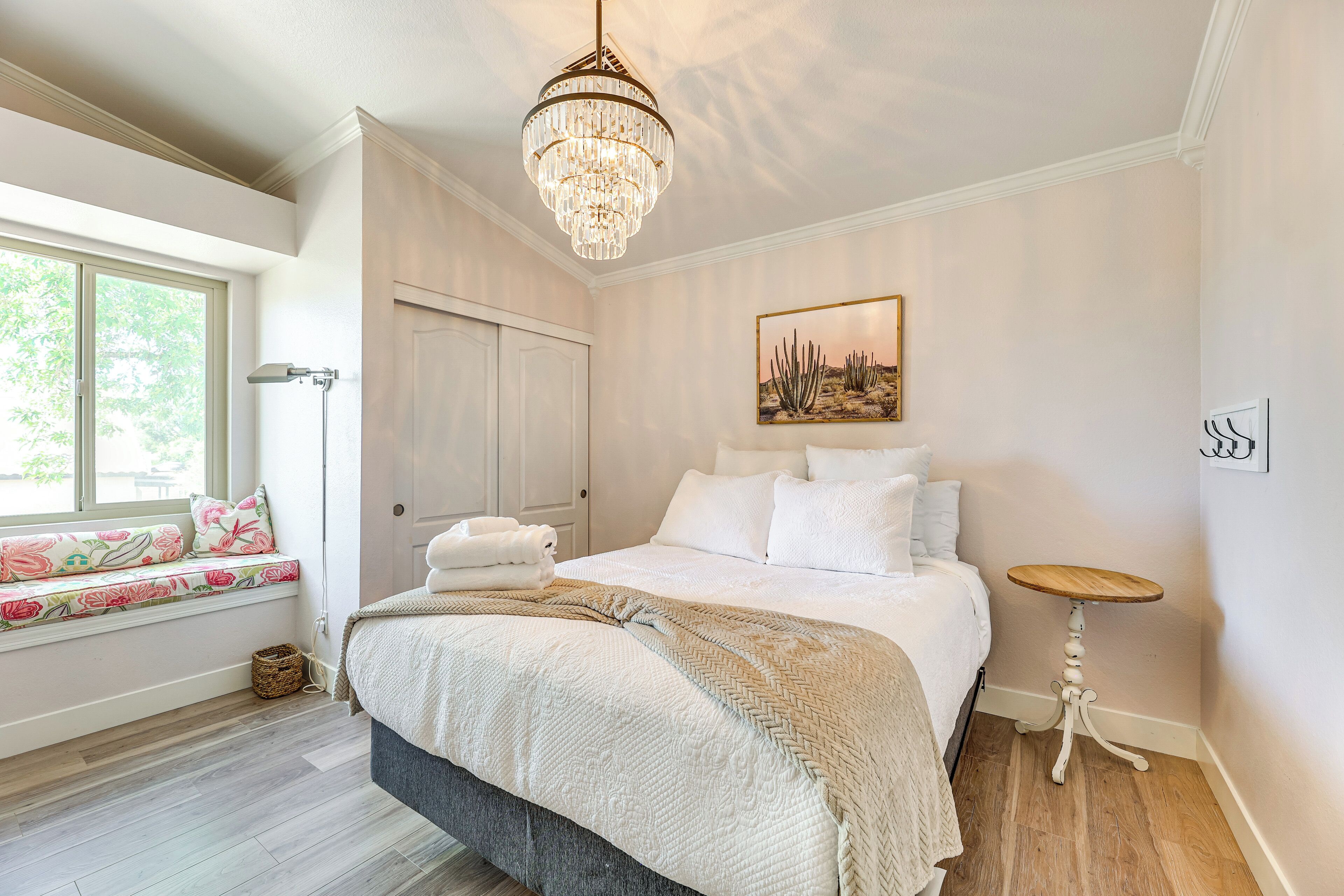 Een slaapkamer met een groot bed, een vensterbank, een kroonluchter en een tafeltje.