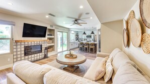 A modern living room with a fireplace, a television mounted on the wall, and a dining area in the background. - Val Vista Lakes Group Getaway: Lake & Pool Access! (Gilbert)