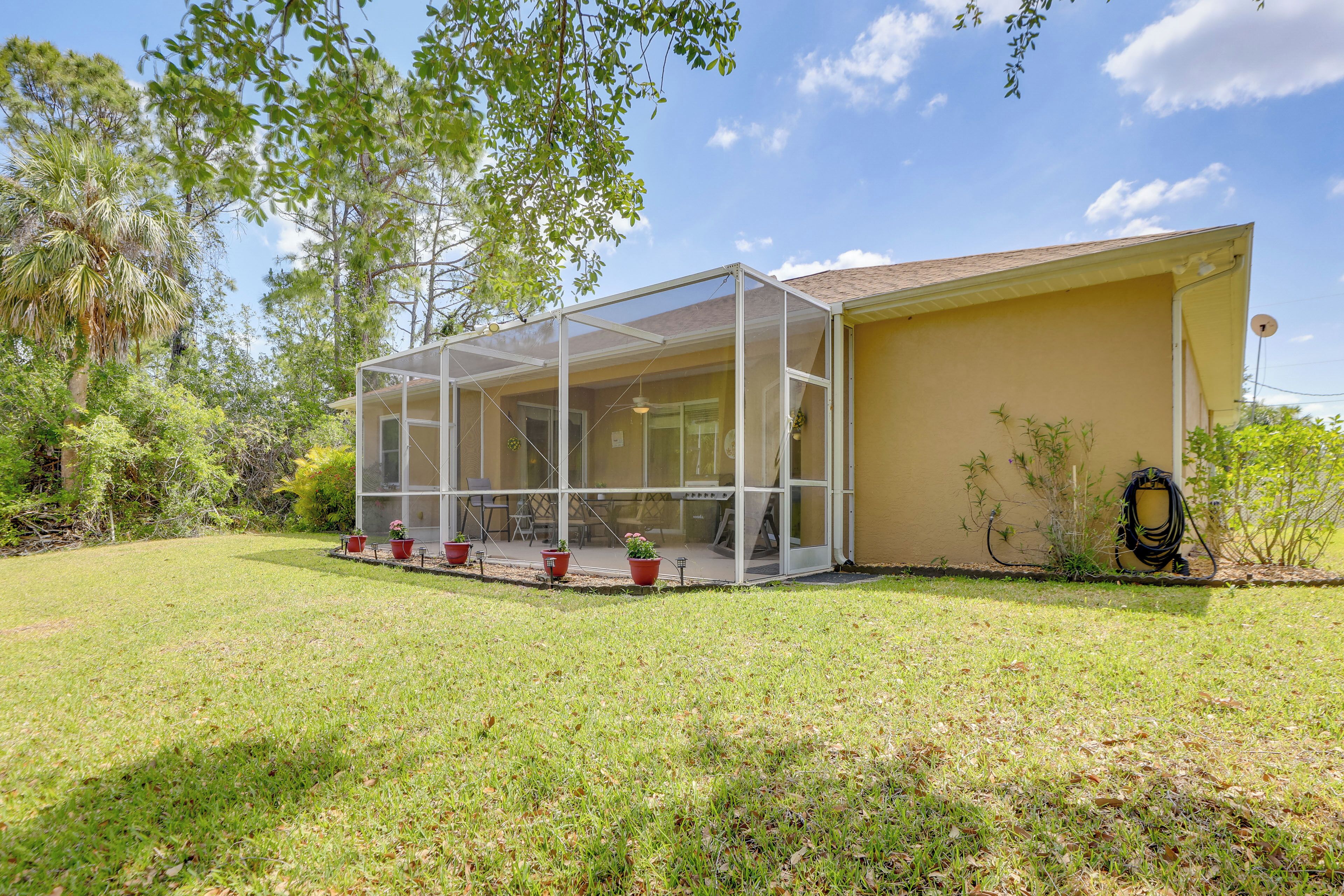 A house with a covered patio area, a lawn, and surrounding trees.