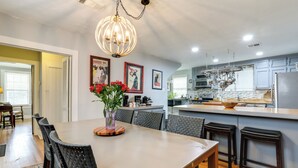 Una cocina moderna con una isla central, iluminación colgante y una zona de comedor con una mesa grande y sillas.