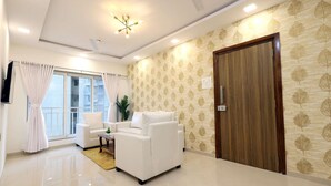 A modern living room with a white sofa set, a wooden door, and a patterned wallpaper. - 3BHK Master Suite (Gagal Home) (Mumbai)