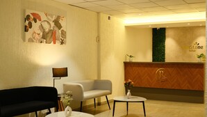 Et reception område med en receptionsdisk, en sort sofa, en hvid sofa og to små borde med vaser.