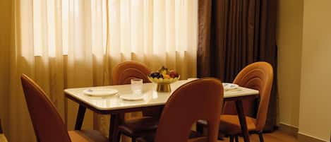 Un comedor con una mesa dispuesta para cuatro personas, sillas, un frutero y un vaso de agua.