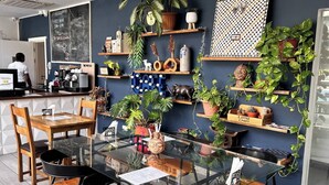 A cafe with a glass table, wooden chairs, and shelves with plants and decorative items. - Comffy Cozzy Studio  Embassy Gardens, Accra (Accra)