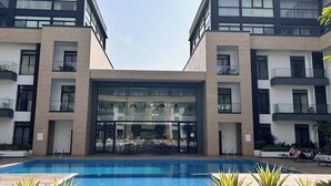A modern building with a central glass facade, a swimming pool, and outdoor seating areas.