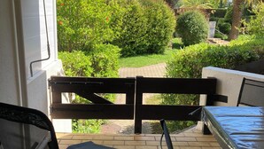 Eine Terrasse im Freien mit Tisch und Stühlen, ein überdachter Bereich mit gestreiftem Markisenstoff und Blick auf einen üppigen Garten mit verschiedenen Pflanzen und Bäumen.