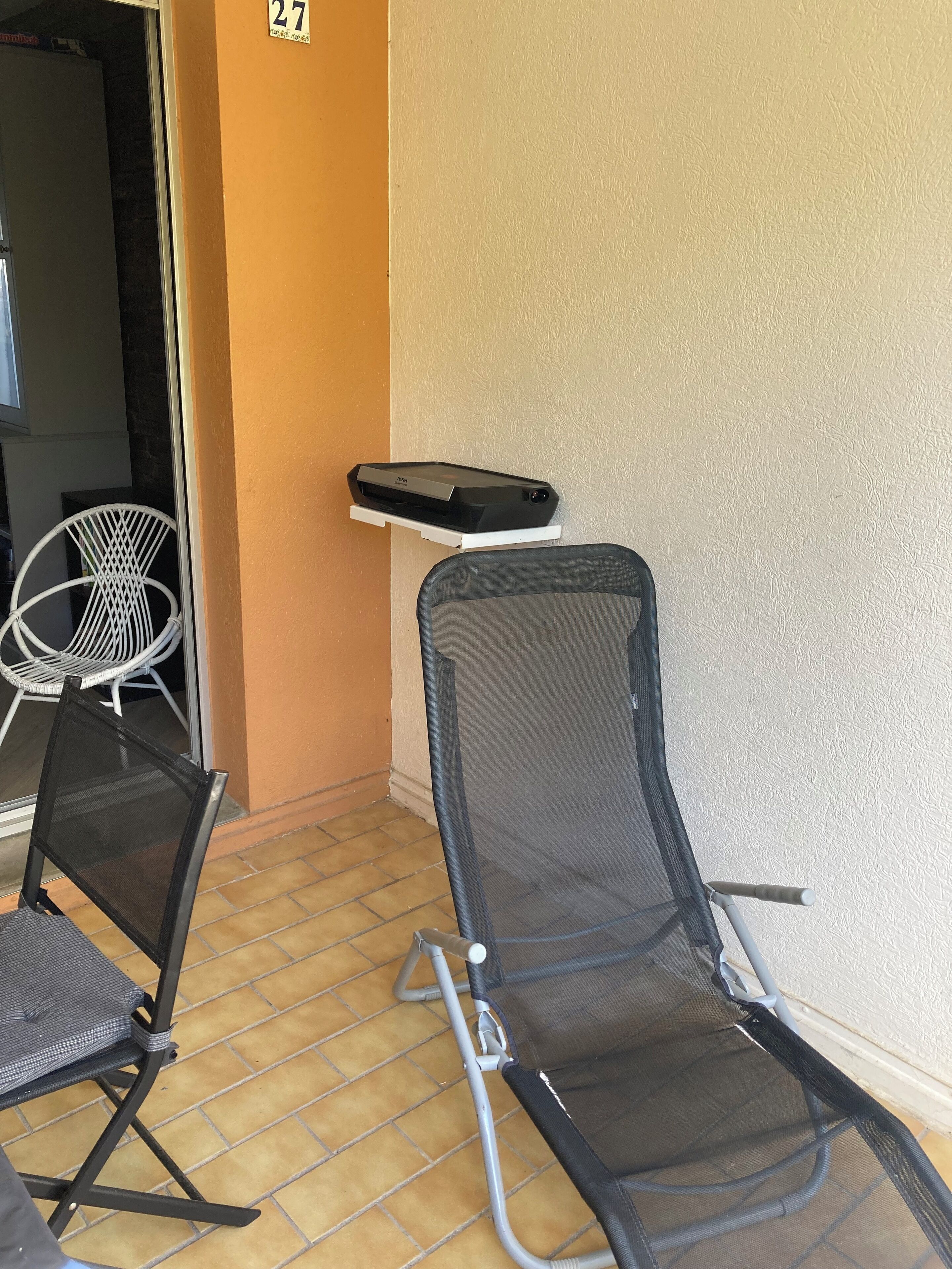 A seating area with two chairs and a small table, a white wall with a number, and a door leading to another room.