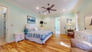 A bedroom with a bed, nightstands, a ceiling fan, a TV, and a door leading to another room. - Little Slice of Paradise (Bolivar Peninsula)