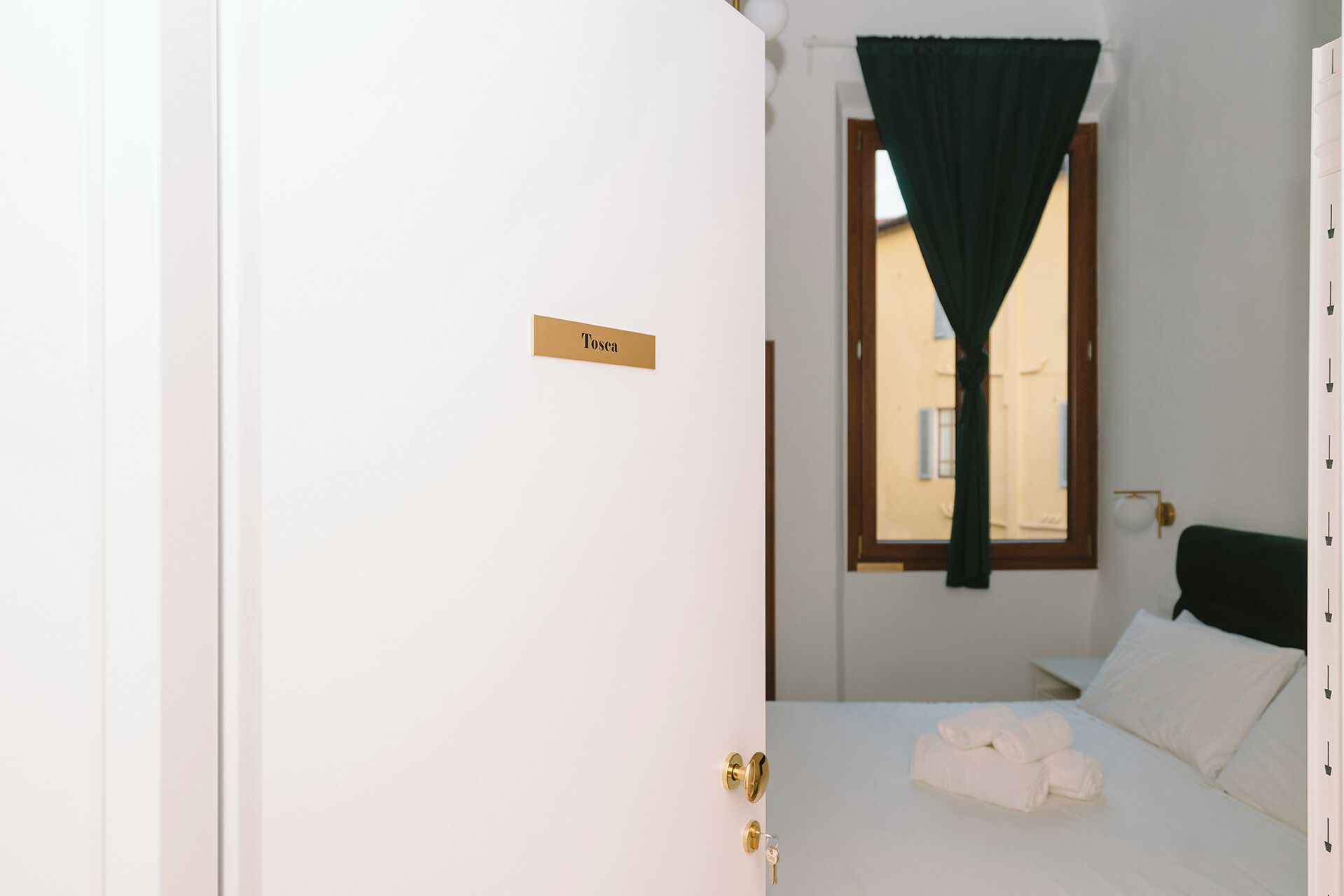 Une chambre d’hôtel avec un lit, une fenêtre avec un rideau, une pancarte sur la porte et une vue sur les bâtiments à l’extérieur.