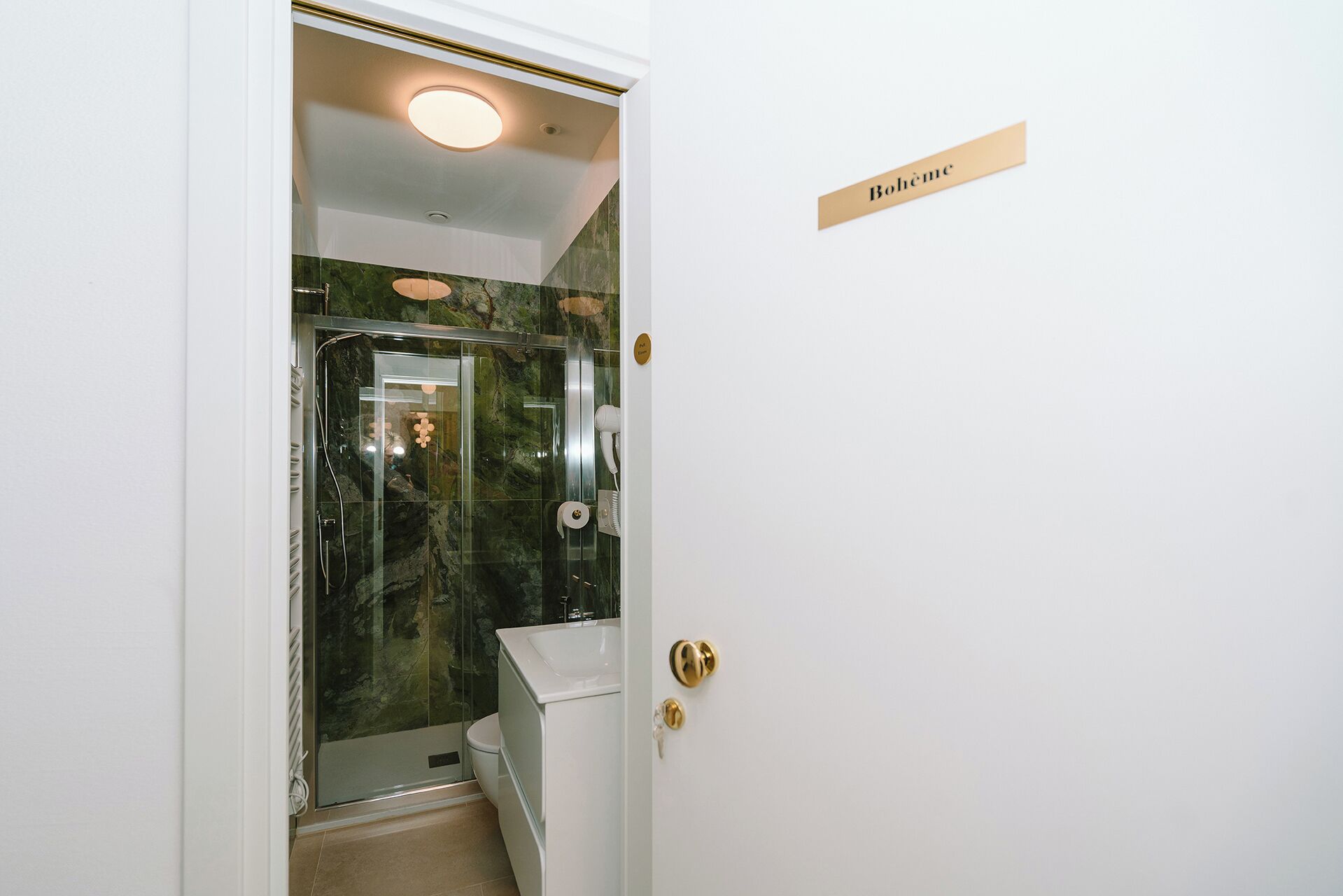 Un baño con cabina de ducha de vidrio, un lavabo blanco y un pomo de puerta dorado.