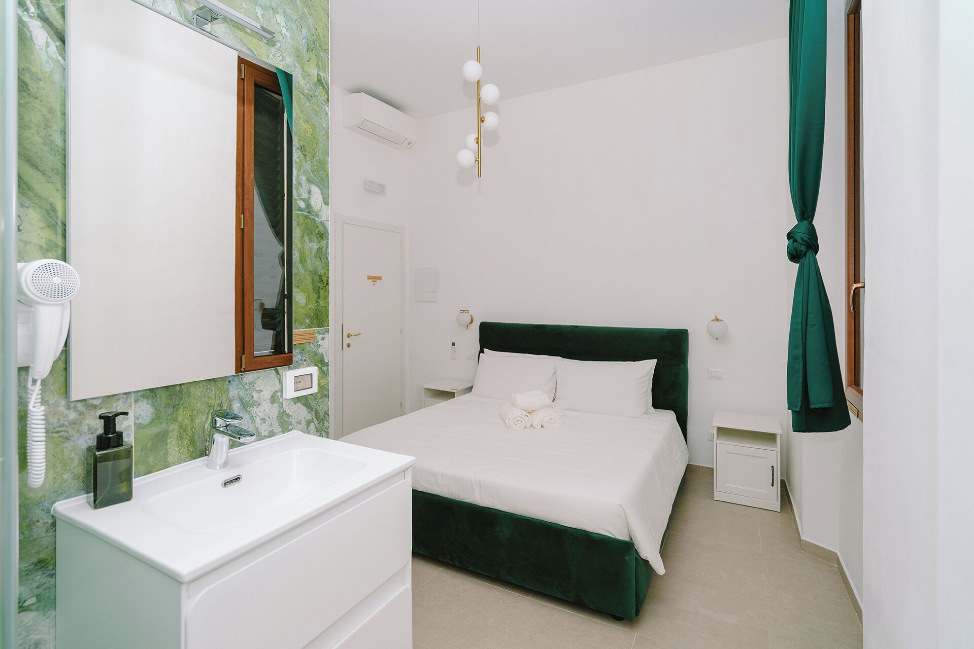 A hotel room with a bed, a vanity with a mirror, a hairdryer, and a green curtain.