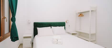 A neatly made bed with white linens, a green headboard, and a white nightstand with a lamp.