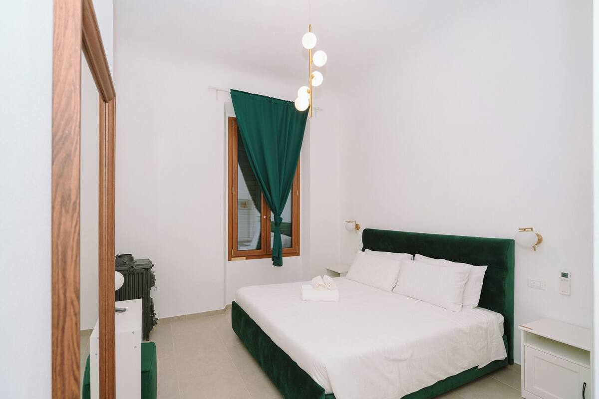 A bedroom with a bed, a mirror, a nightstand, and a wall-mounted light fixture.