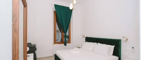 A bedroom with a bed, a mirror, a nightstand, and a wall-mounted light fixture.